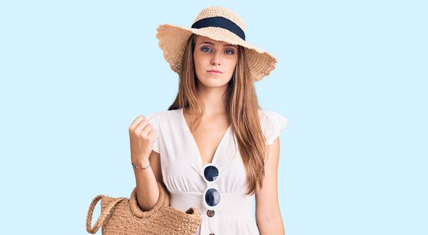 Young beautiful blonde woman wearing summer dress and wicker handbag thinking attitude and sober expression looking self confident  - Zdjęcie, obraz