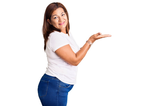 Középkorú latin nő viselése alkalmi fehér póló mutatott félre a kezét nyitott tenyér mutatja másolás tér, bemutató reklám mosolygó izgatott boldog  - Fotó, kép