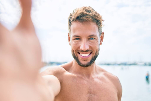Bonito homem caucasiano fitness na praia em um dia ensolarado tirar uma foto selfie - Foto, Imagem