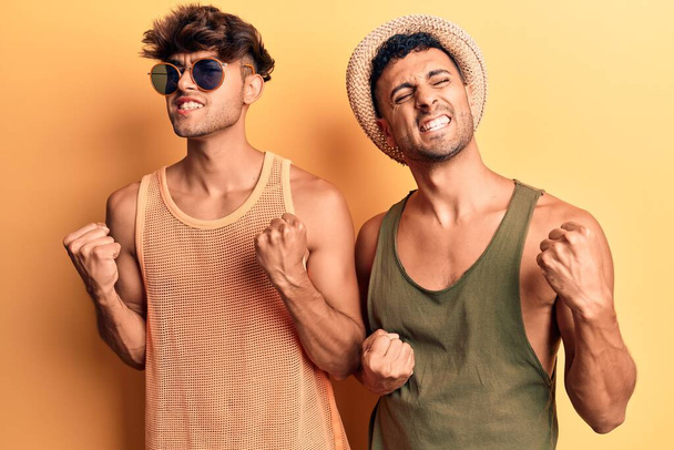 Young gay couple wearing summer clothes excited for success with arms raised and eyes closed celebrating victory smiling. winner concept.  - Foto, Imagen