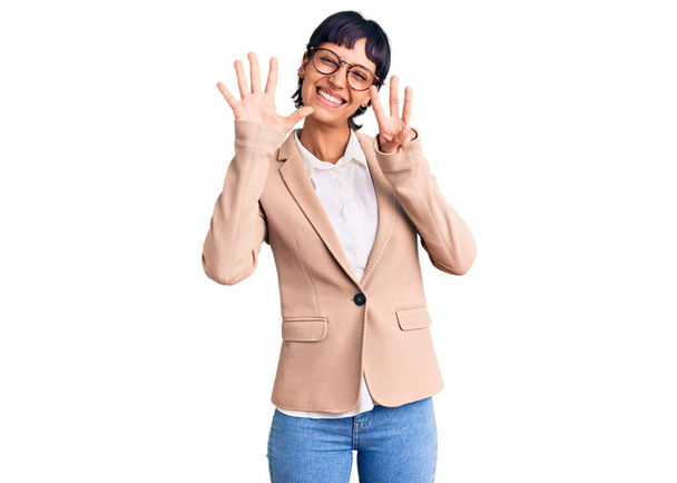 Mulher morena jovem com cabelo curto vestindo jaqueta de negócios e óculos mostrando e apontando para cima com os dedos número oito enquanto sorri confiante e feliz.  - Foto, Imagem