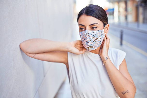 Beautiful young woman wearing fashionable clothes and colorful medical safety mask for coronavirus walking down the street - Фото, изображение