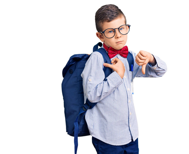 Cute blond kid wearing nerd bow tie and backpack with angry face, negative sign showing dislike with thumbs down, rejection concept  - Fotó, kép