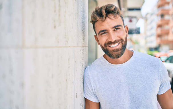 Nuori latino mies hymyilee onnellinen nojaten seinään kaupungin - Valokuva, kuva