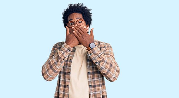 Handsome african american man with afro hair wearing casual clothes and glasses shocked covering mouth with hands for mistake. secret concept.  - Fotó, kép