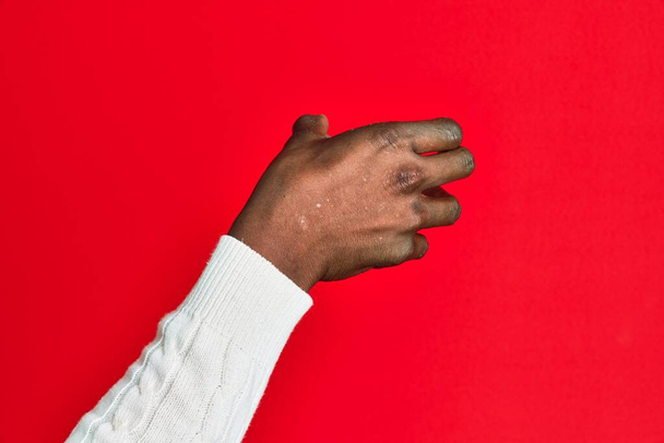 Arm and hand of african american black young man over red isolated background holding invisible object, empty hand doing clipping and grabbing gesture  - Fotó, kép