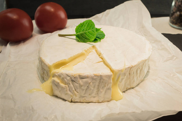 Trancher une tranche de fromage Camembert. Fromage rond et feuilles de menthe fraîche - Photo, image