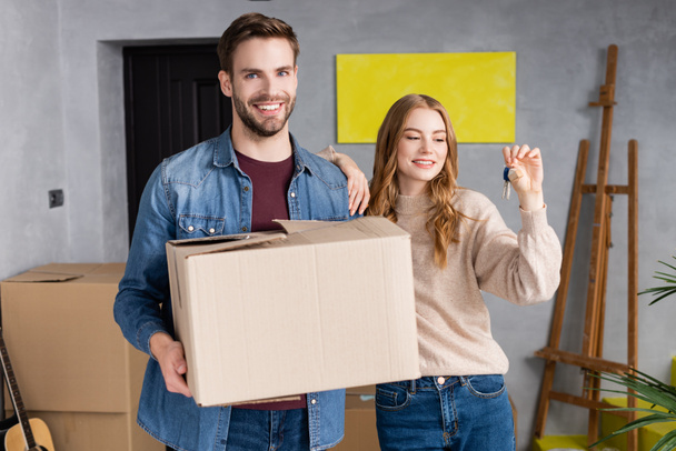 joyful woman looking at keys near boyfriend holding carton box  - Photo, Image