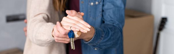 panoramic crop of man and woman holding hands and keys, moving concept - Foto, imagen