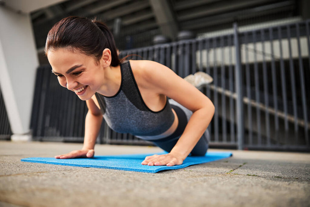 Vrolijke jonge vrouw genieten van workout op mat - Foto, afbeelding