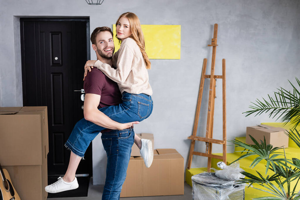 joyful man holding in arms pleased girlfriend in new home - Fotoğraf, Görsel
