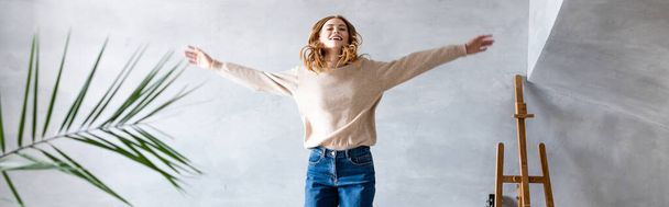 panoramic crop of pleased woman with outstretched hands jumping in new home, relocation concept - Foto, Imagen