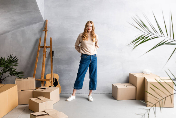 young woman standing near carton boxes and acoustic guitar, relocation concept - Photo, Image