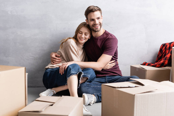 pleased man sitting of floor and hugging woman near boxes - Fotó, kép