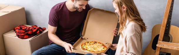 カートンボックスのピザを見る男性と女性のパノラマの概念 - 写真・画像