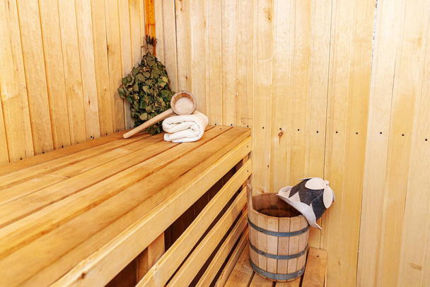 Interior details Finnish sauna steam room with traditional sauna accessories basin birch broom scoop felt hat towel. Traditional old Russian bathhouse SPA Concept. Relax country village bath concept - Photo, Image