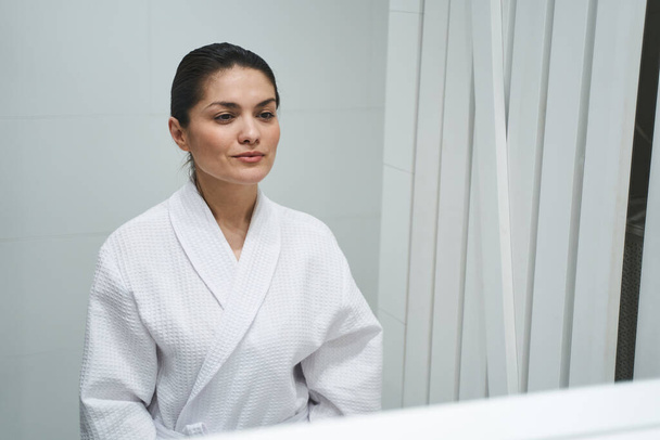 Woman dressed in a bathrobe standing in a bathroom - Фото, зображення