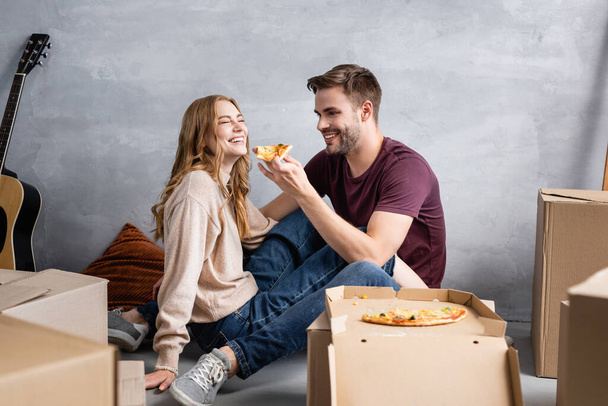 selective focus of joyful man holding delicious pizza near girlfriend and carton boxes, moving concept - Valokuva, kuva