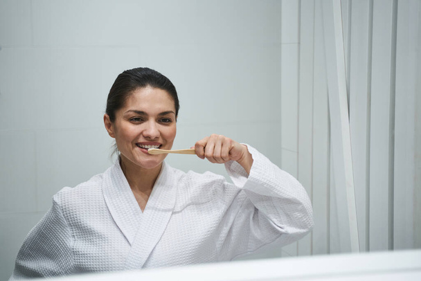 Pleased lady cleaning her teeth in the bathroom - Фото, зображення