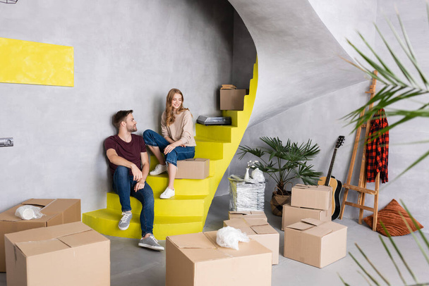 Paar sitzt auf Treppen in der Nähe von Boxen, Akustikgitarre und Staffelei, Umzugskonzept  - Foto, Bild