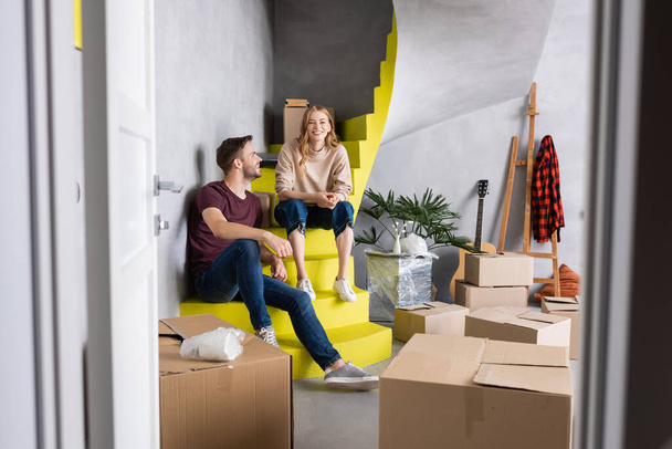 enfoque selectivo de la mujer joven y el hombre sentado en las escaleras cerca de cajas, concepto de reubicación  - Foto, Imagen