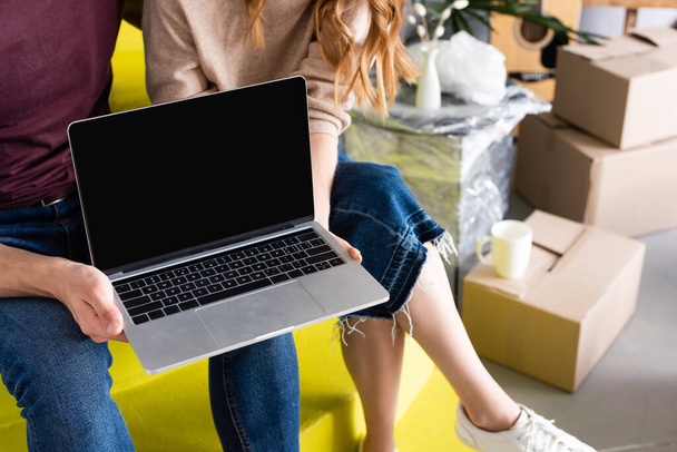 bijgesneden weergave van paar houden laptop met blanco scherm tijdens het zitten op trappen in de buurt van dozen, verhuizing concept  - Foto, afbeelding