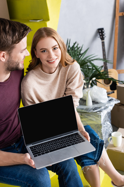 Mann blickt freudige Frau an, während er Laptop mit leerem Bildschirm hält - Foto, Bild