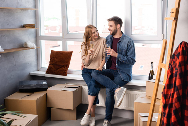 pleased woman and man holding glasses with champagne near carton boxes - Foto, Imagen