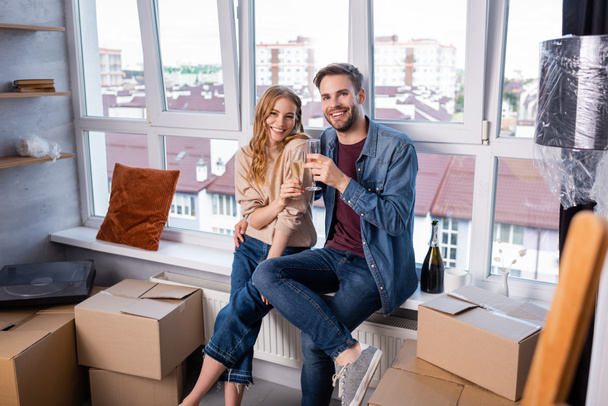 selective focus of pleased couple toasting glasses with champagne near carton boxes, moving concept  - Photo, Image