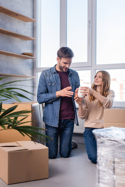 man looking at cup in hands of woman while unpacking carton boxes in new home, moving concept - Fotografie, Obrázek