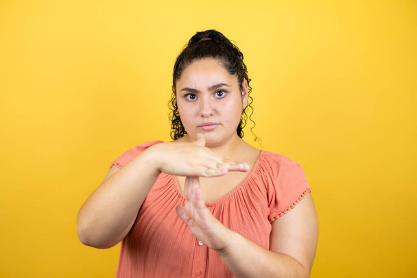 Młoda piękna kobieta z kręconymi włosami na odizolowanym żółtym tle Wykonując gest dłońmi, sfrustrowana i poważna twarz - Zdjęcie, obraz