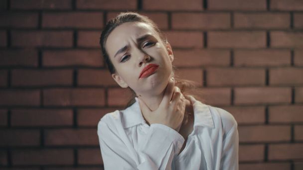 Mutsuz kadın boğaz ağrısı çekiyor ve duvarda öksürüyor. - Fotoğraf, Görsel