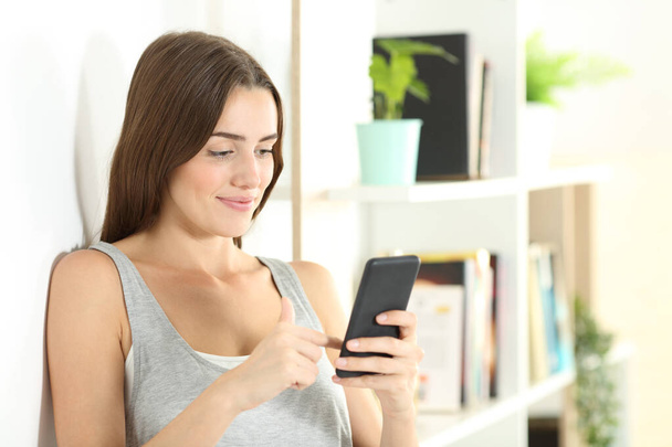 Akıllı telefon kullanan gülen kız evdeki oturma odasında internetten içeriğini kontrol ediyor. - Fotoğraf, Görsel