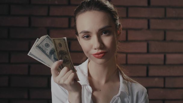 Hochmütige Frau blickt in die Kamera und zeigt Geldstapel für Geldstapel an Ziegelmauer - Foto, Bild