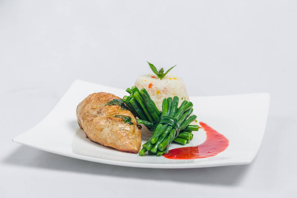 Pácolt csirkemell hosszú zöldbabbal és könnyű zöldséges rizs tálcával. Étel dekoráció piros mártással egy fehér tányéron. Elszigetelt fehér háttér. - Fotó, kép