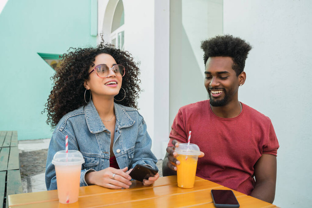 Portrait of two Afro friends having fun together and enjoying good time while drinking fresh fruit juice outdoors at cafeteria. - Фото, изображение