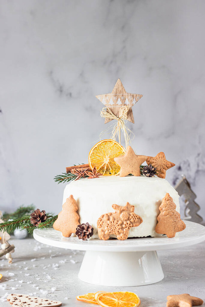Christmas or New Year gingerbread cake with white cream decorated with gingerbread cookies, fir tree branches, cones, spices and dried orange. Winter cake. Grey concrete background. - Fotoğraf, Görsel