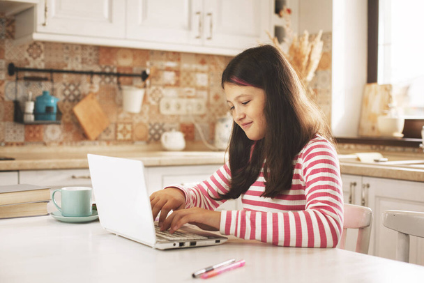 Chica adolescente viendo video tutorial en la computadora portátil en la cocina, aprendizaje a distancia, educación en línea, concepto de aprendizaje en el hogar - Foto, imagen