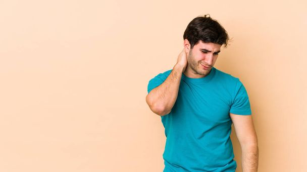 Young man isolated on beige background having a neck pain due to stress, massaging and touching it with hand. - Fotoğraf, Görsel