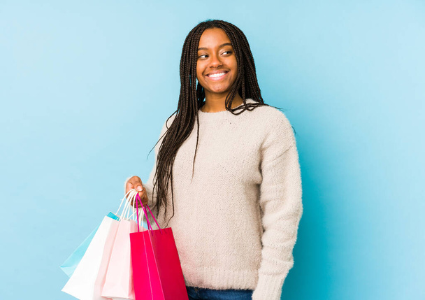 Młoda Afroamerykanka trzymająca torbę na zakupy wygląda na uśmiechniętą, wesołą i miłą. - Zdjęcie, obraz