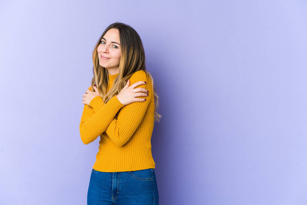 Young caucasian woman isolated on purple background hugs, smiling carefree and happy. - Fotografie, Obrázek