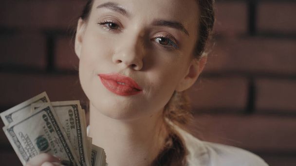 Mulher sexy mostrando dinheiro em dinheiro e olhando para a câmera no estúdio de tijolo - Foto, Imagem