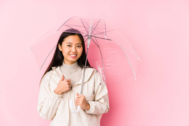Young chinese woman holding a umbrella isolated smiling and raising thumb up - Zdjęcie, obraz