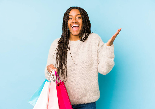 Giovane donna afroamericana che tiene una shopping bag isolata ricevendo una piacevole sorpresa, eccitata e alzando le mani. - Foto, immagini
