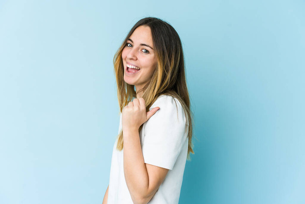Young caucasian woman isolated on blue background points with thumb finger away, laughing and carefree. - Photo, Image