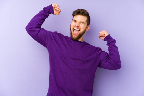 Молодий кавказький чоловік ізольований на фіолетовому фоні, святкуючи особливий день, стрибає і піднімає руки з енергією
. - Фото, зображення