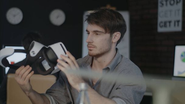 Young man holding virtual reality goggles in creative dark office - Photo, Image