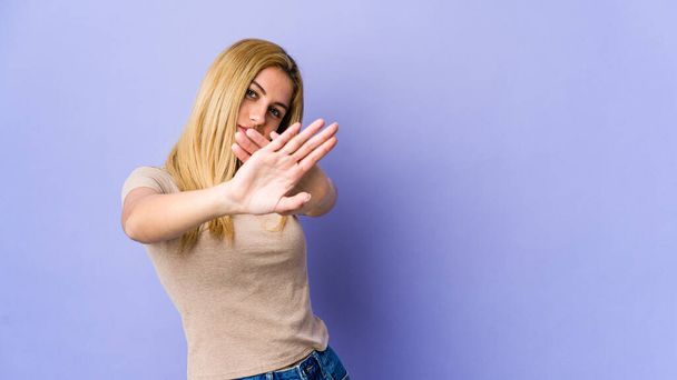 Young blonde woman isolated on purple background standing with outstretched hand showing stop sign, preventing you. - Photo, Image