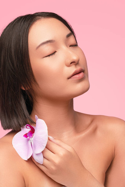 Asian model caressing shoulder with orchid - Фото, изображение