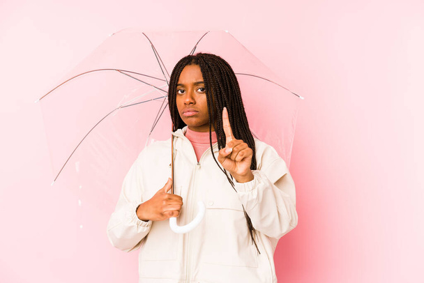 Junge afrikanisch-amerikanische Frau hält isoliert einen Regenschirm und zeigt die Nummer eins mit dem Finger. - Foto, Bild